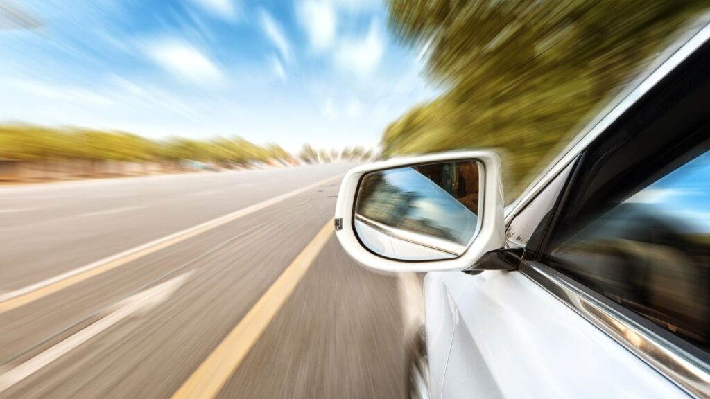 A speeding car's sideview mirror, with images zoomed for a fast moving effect. 
