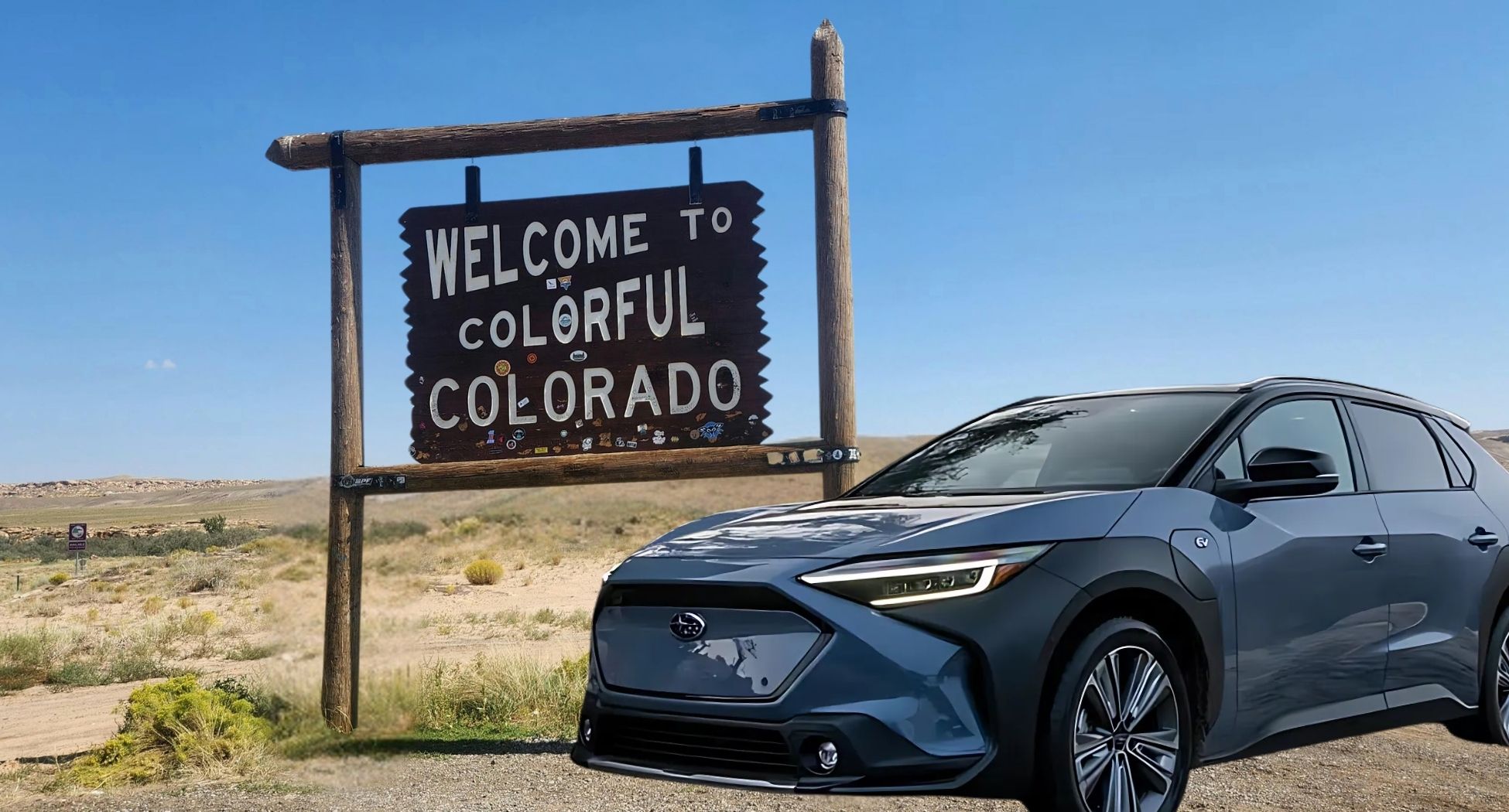 Blue and black electric Subaru in front of a wooden sign that says "Welcome to Colorful Colorado"
