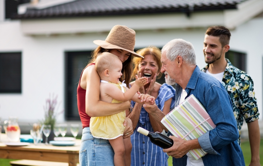 A multigenerational family gathers outdoors as a mother holds her baby while the child interacts with an older family member.
