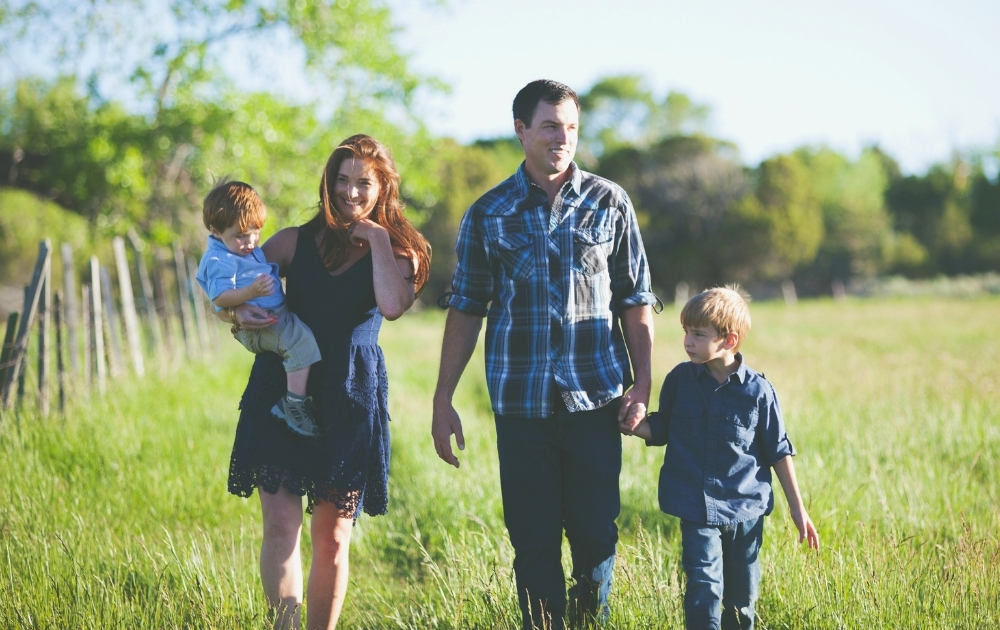 Baby Bonds Colorado A family with two young children walks together through a grassy field on a sunny day.